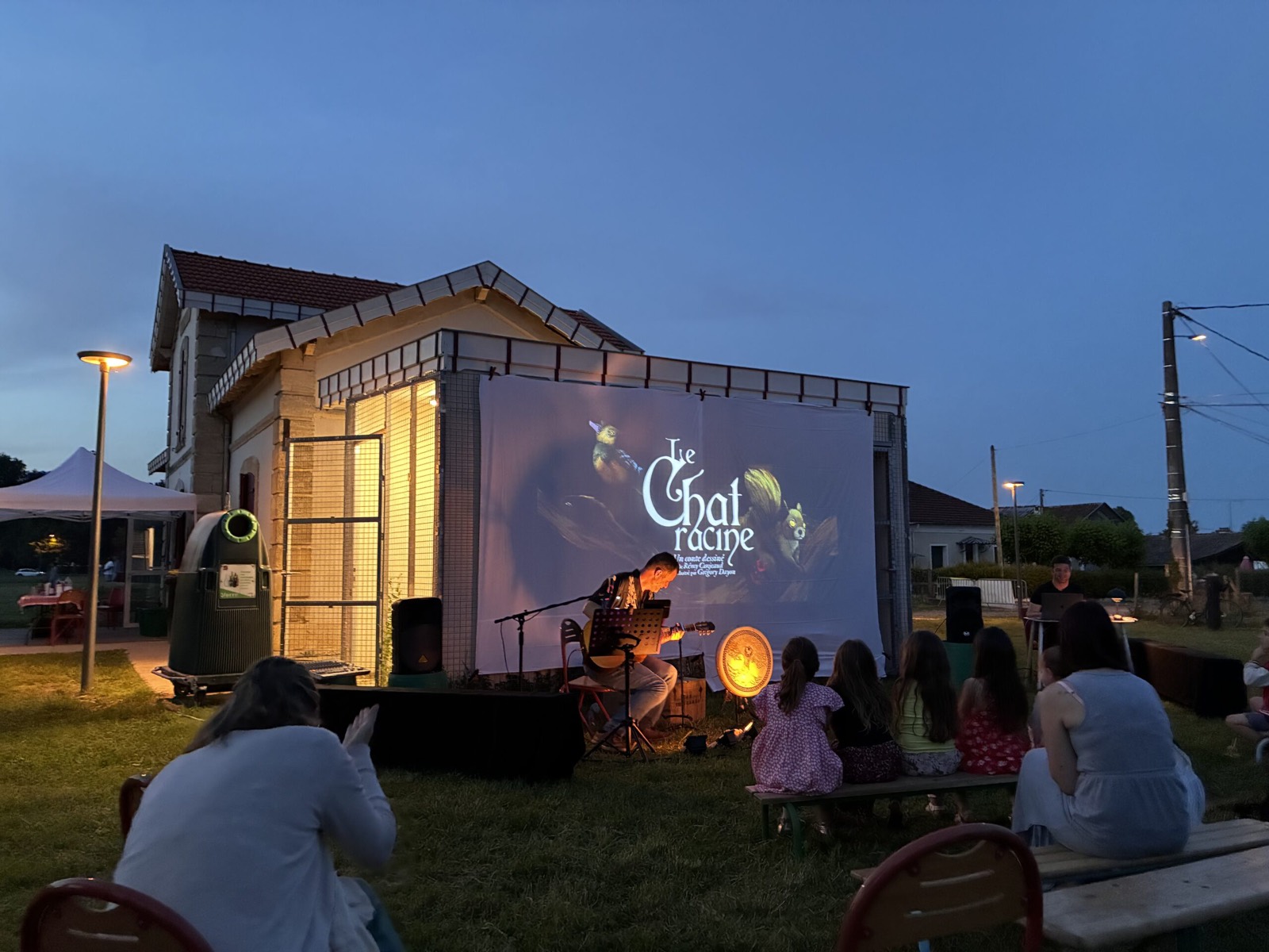 Le spectacle au crépuscule : le titre projeté en grand, le conteur-musicien en scène devant le public