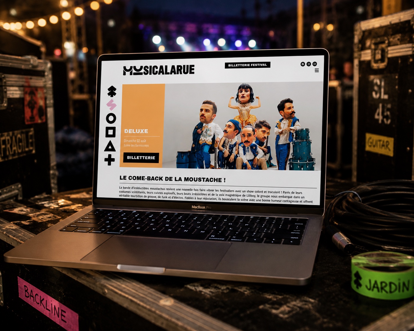 Le site du festival Musicalarue affiché sur un ordinateur portable posé sur les flight cases, scène illuminée en arrière-plan