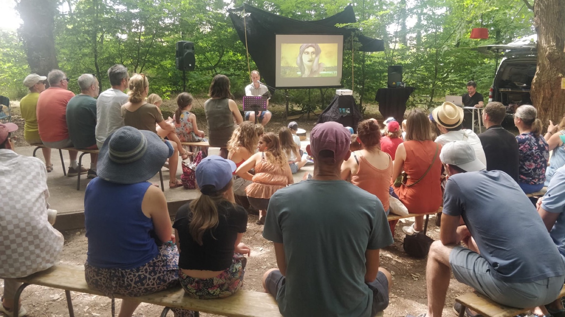 Le public du Chat Racine installé en forêt devant l'écran de projection, Rémy Conjeaud au récit et Grégory Dayon aux images animées en direct