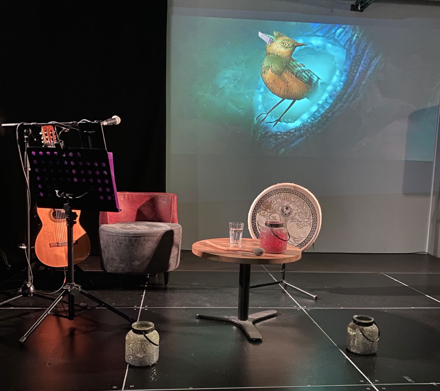La scène du spectacle : guitare, tambour et fauteuil du conteur devant l'oiseau illustré projeté en grand