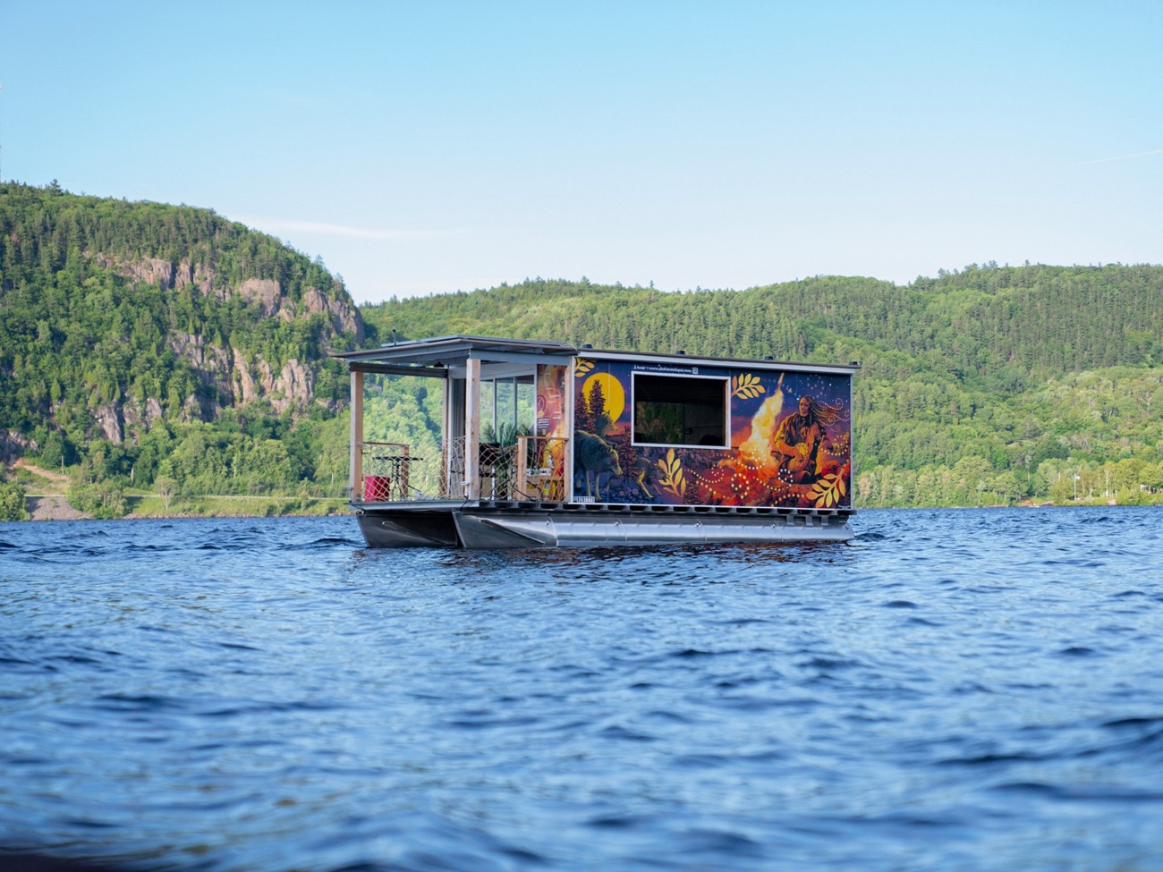 La fresque de la légende de Moowis peinte sur un hébergement flottant, sur la rivière Saint-Maurice au Québec — un récit déployé dans un lieu